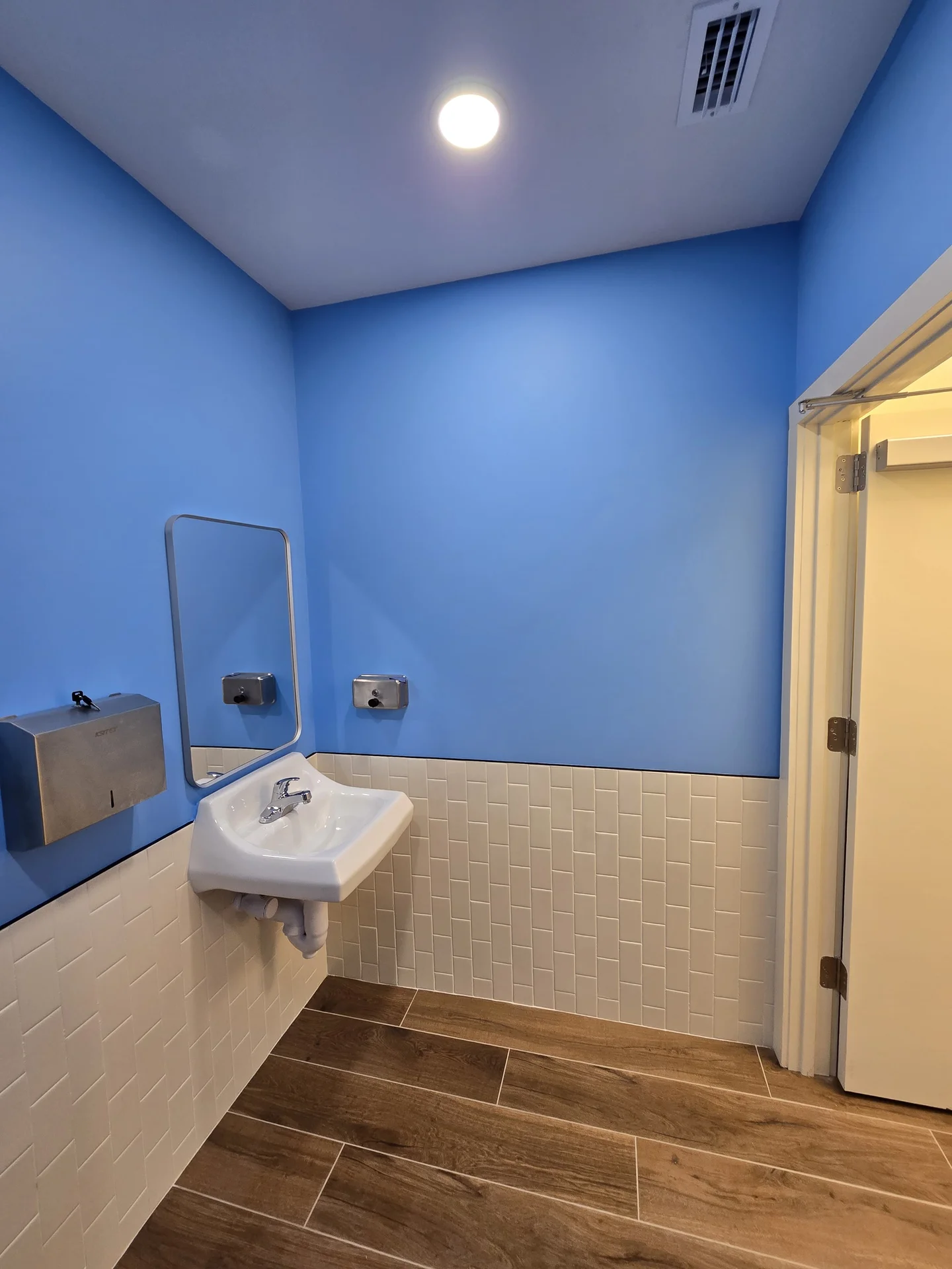 Finished restroom with light-blue walls, white subway-tile wainscot, and wood-look tile floor